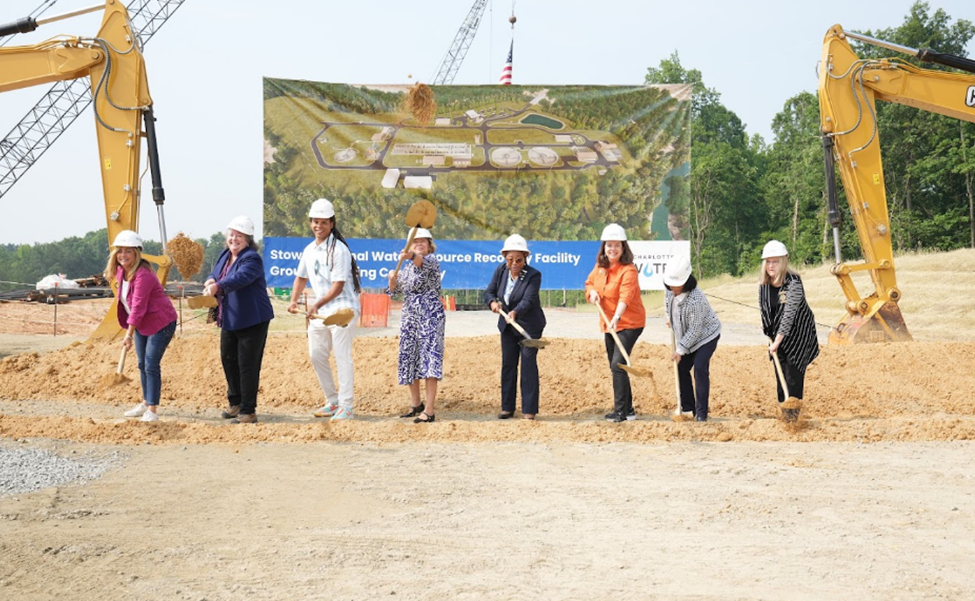 8 community representatives break ground on the new Stowe Regional Water Resource Recovery Facility by wearing hard hats and digging into the ground on the construction site.