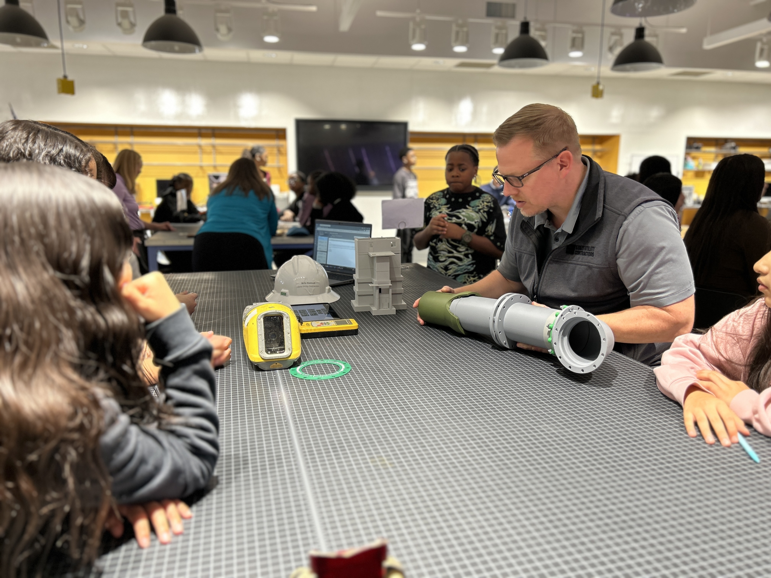 Students around a lab table look at pipes and survey equipment