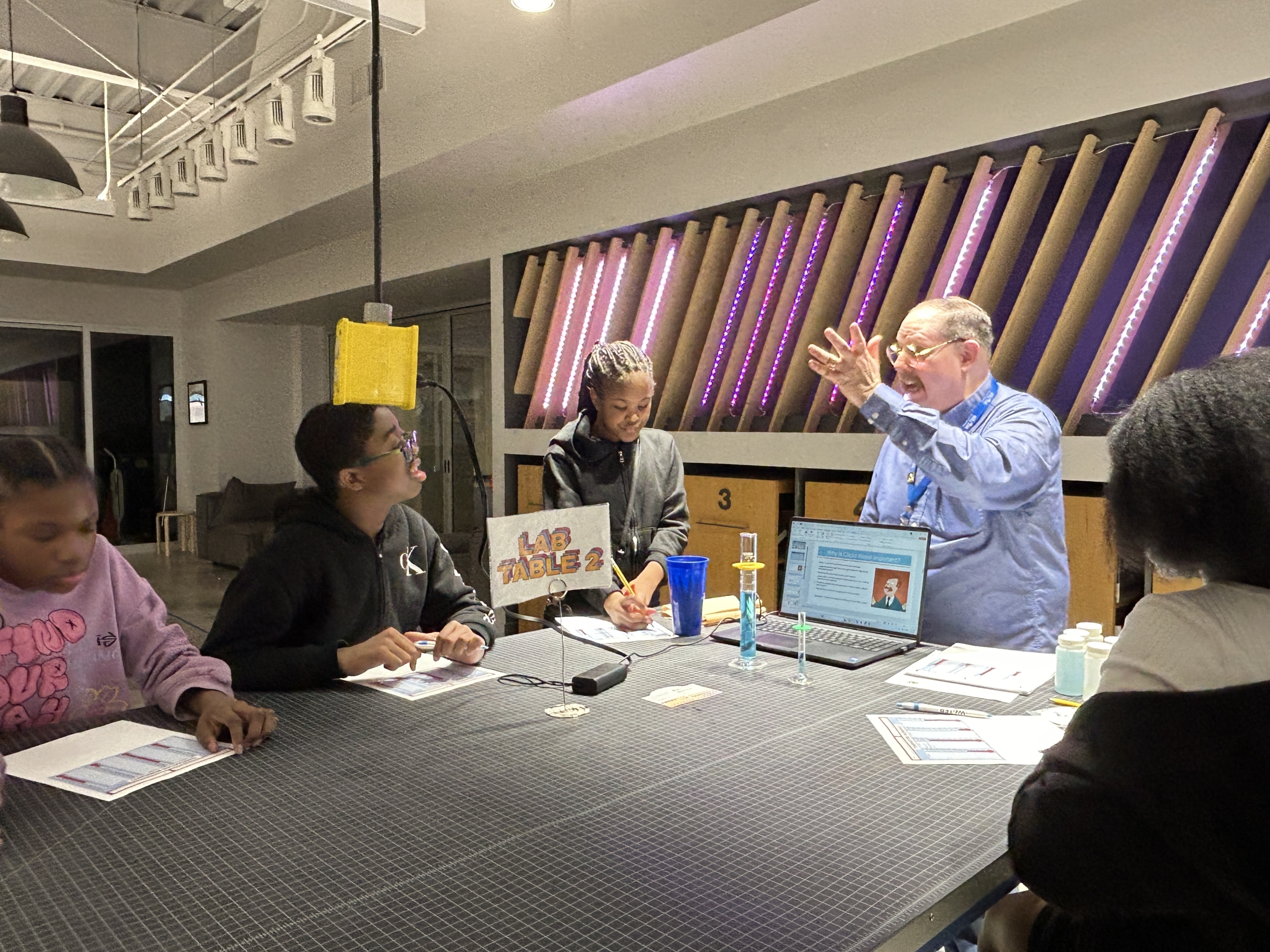  A Charlotte Water lab employee excitedly speaks to students with lab kits on the table.