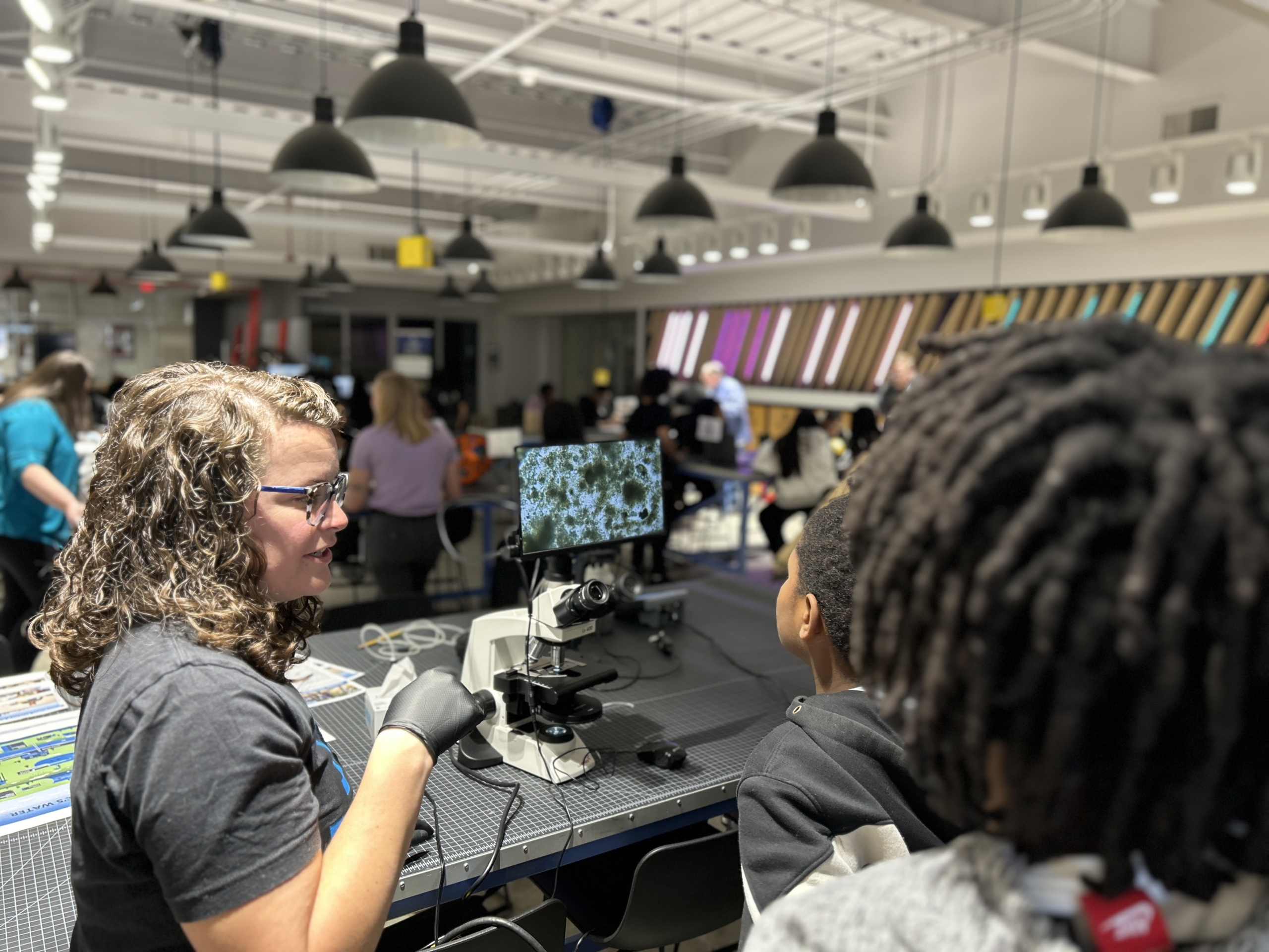 Students gather around the display screen of a microscope with a Charlotte Water employee
