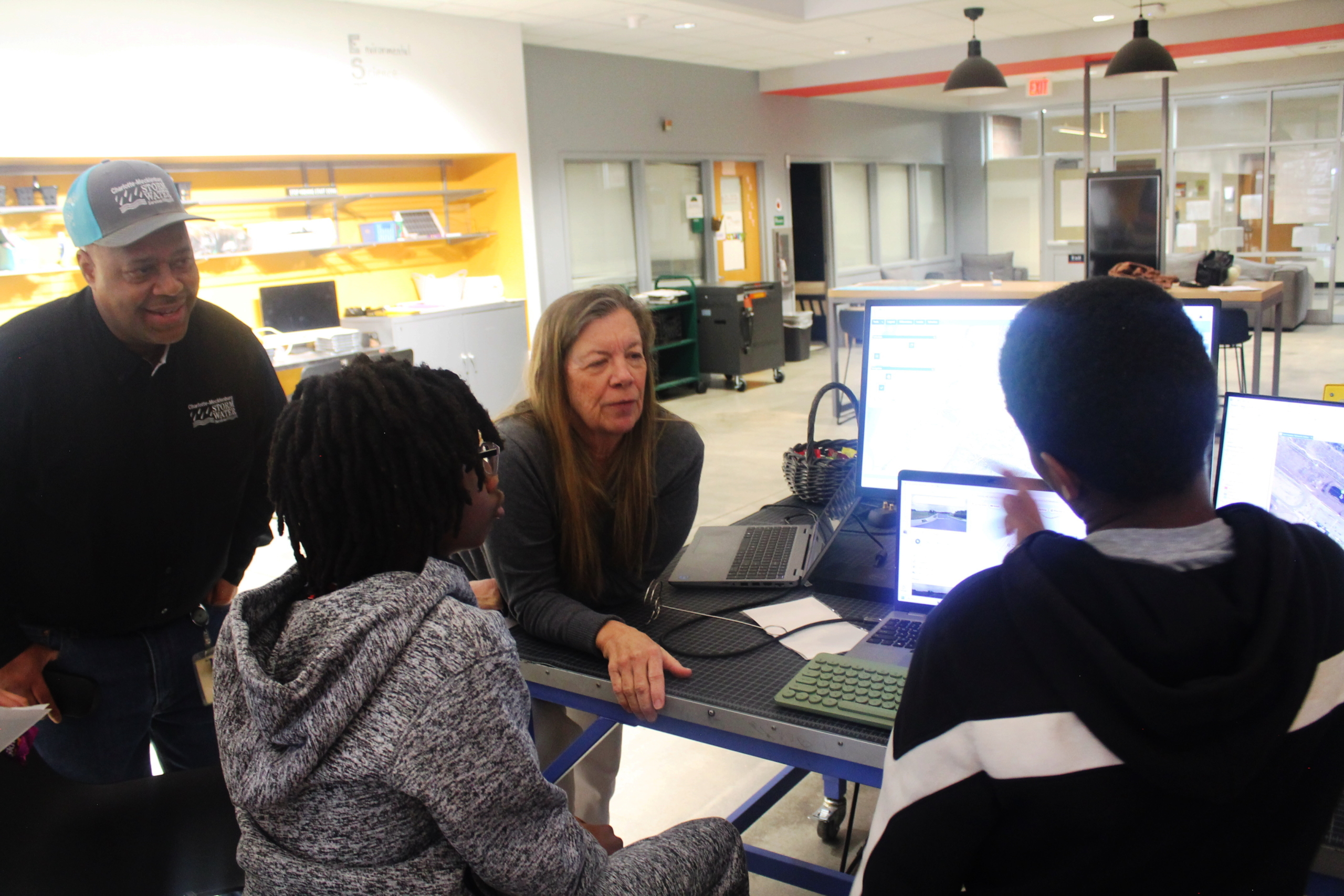 A student points to a monitor asking questions of two Stormwater employees.