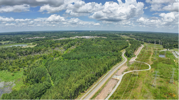 A paved road cutting through a tree line paralleled by a multi-use path.