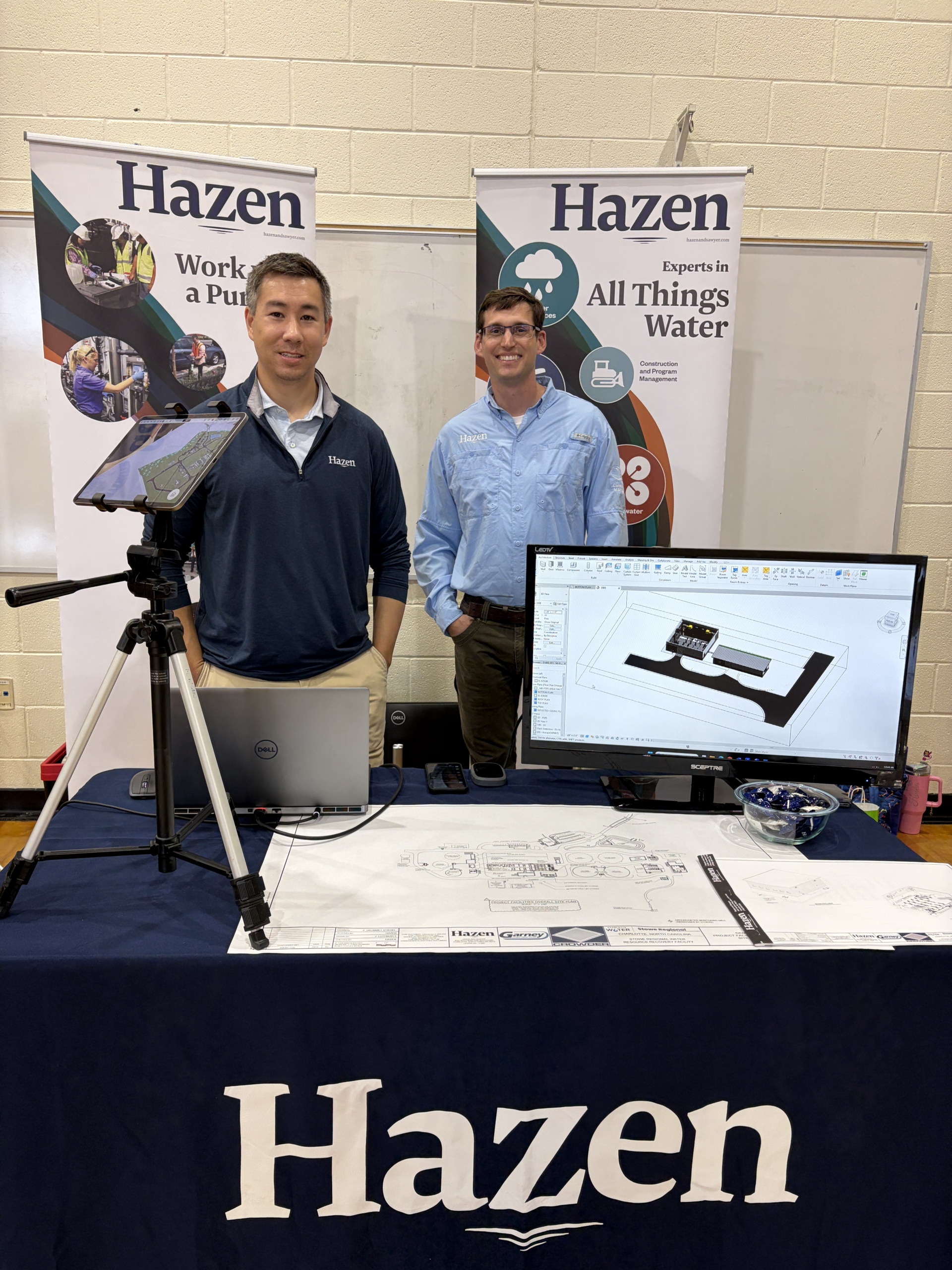 Engineers from Hazen smile behind a table set with computer screens and blueprints.