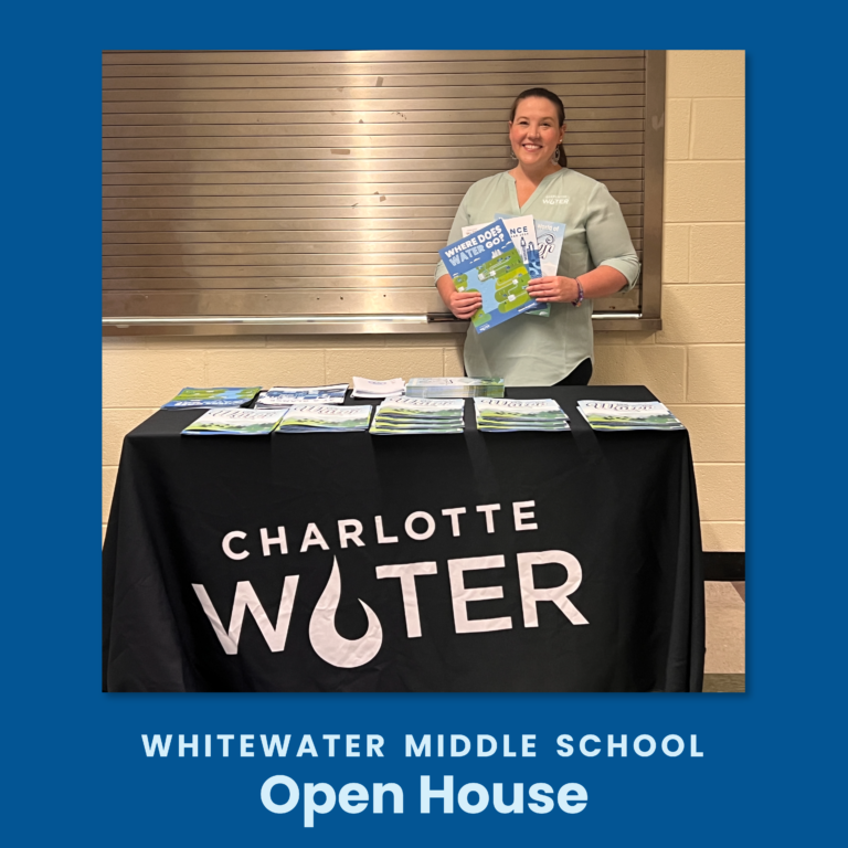 Project Manager Nicole Bartlett poses at a Charlotte Water table with activity books. Caption Whitewater Middle School Open House.