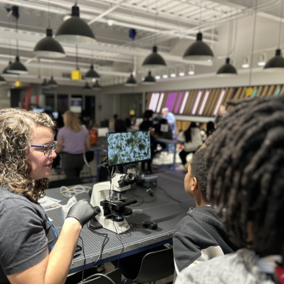 Students gather around the display screen of a microscope with a Charlotte Water employee