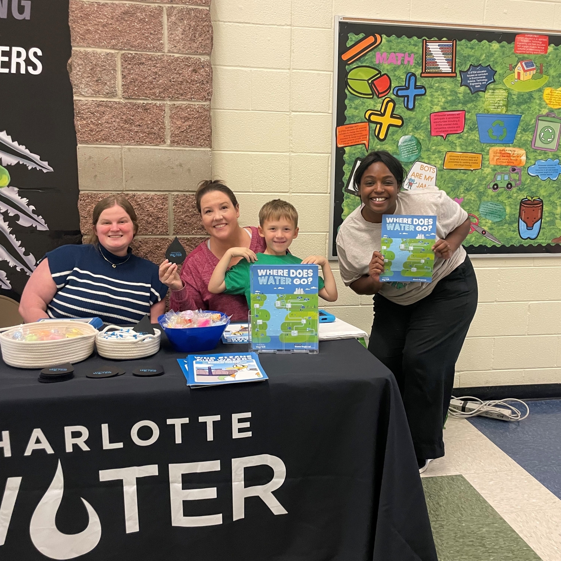 Three women and a child sitting at a Charlotte Water table with brochures.